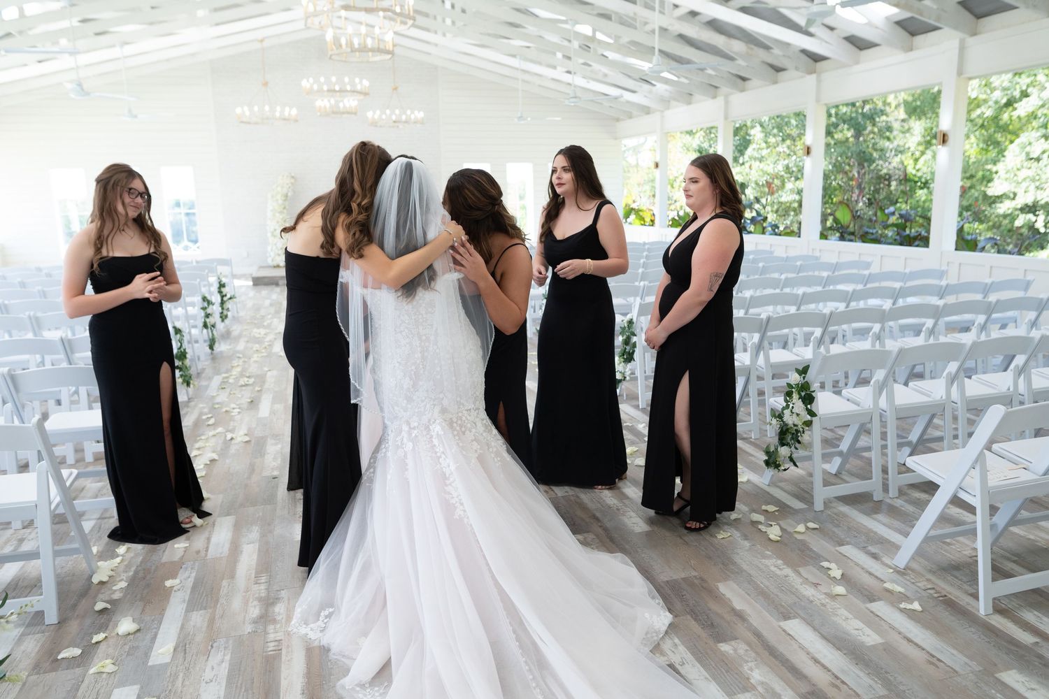 A group of bridesmaids in black dresses stand together with a bride in white during a wedding celebration.