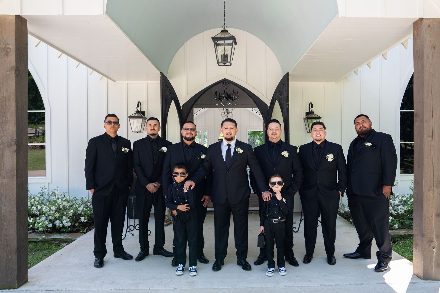 A group of people wearing matching black suits stand in an elegant archway entrance with white columns.