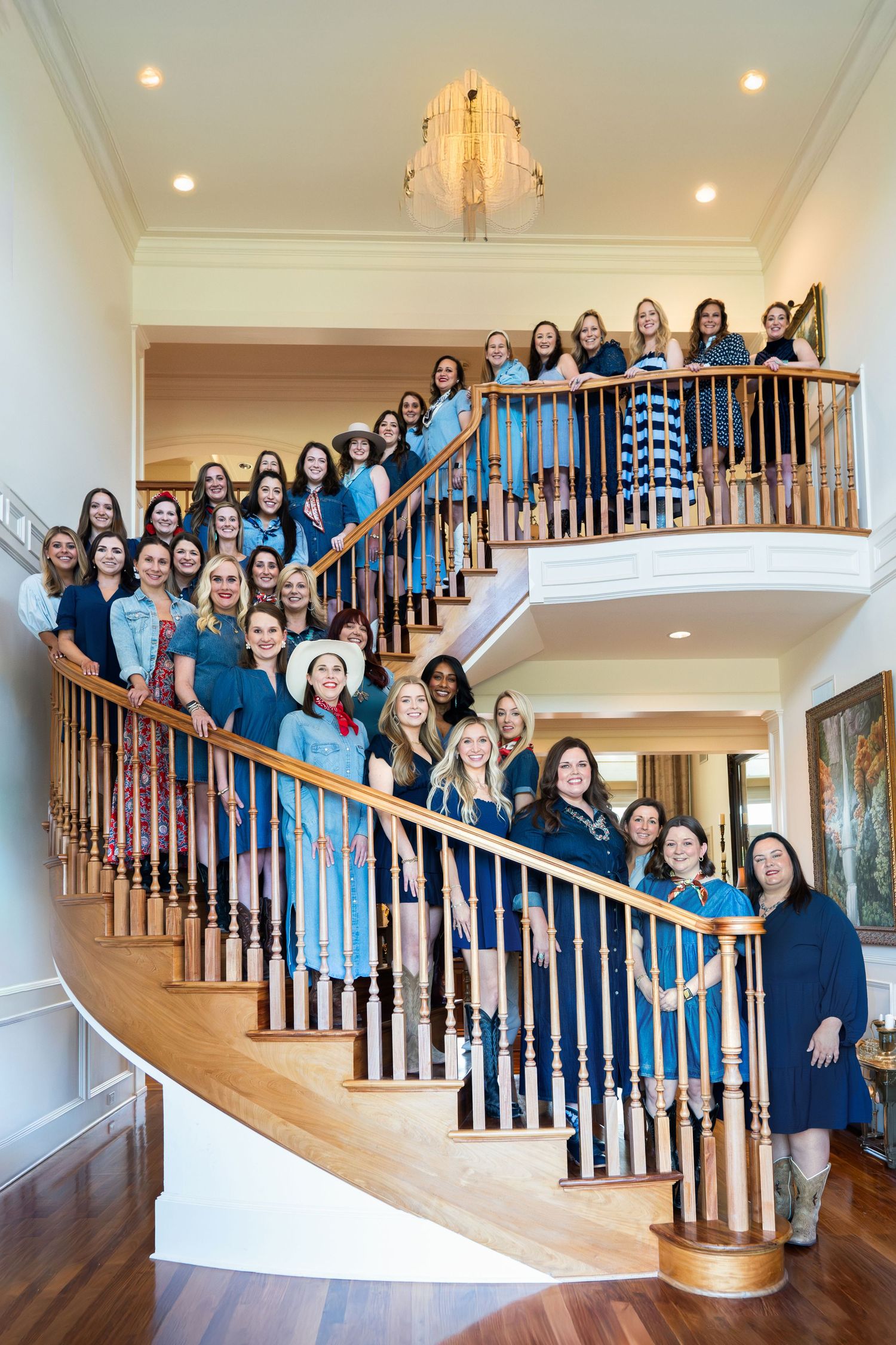 A large group of people in coordinated outfits pose together on an elegant staircase for a formal photo.