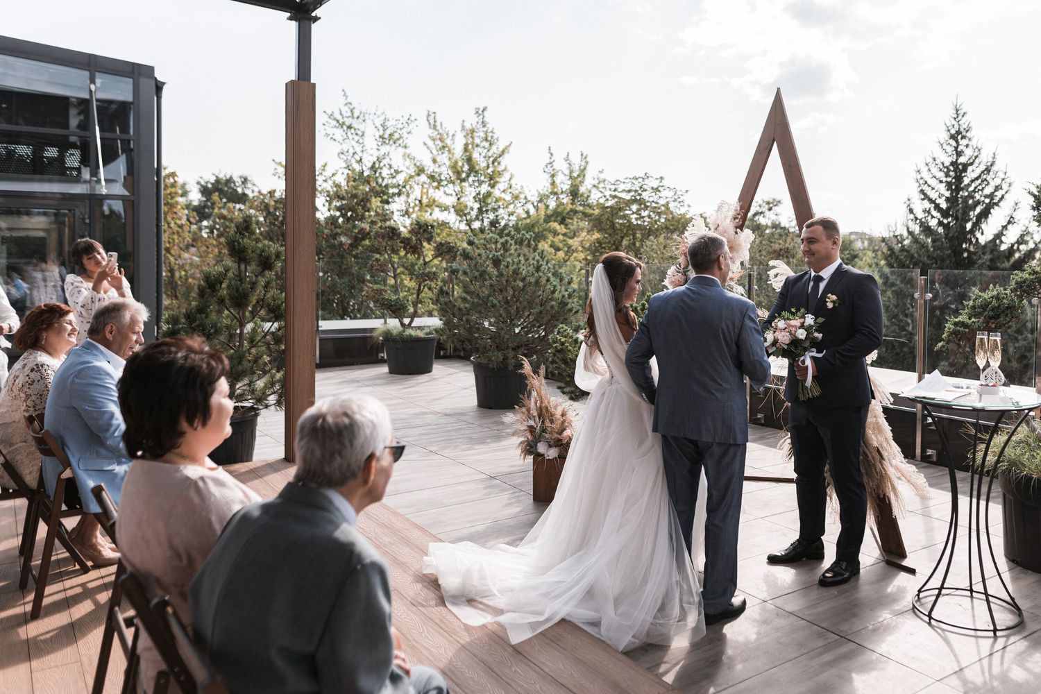 A series of wedding photos showing guests and a bride in an outdoor venue with wooden beams and natural scenery.