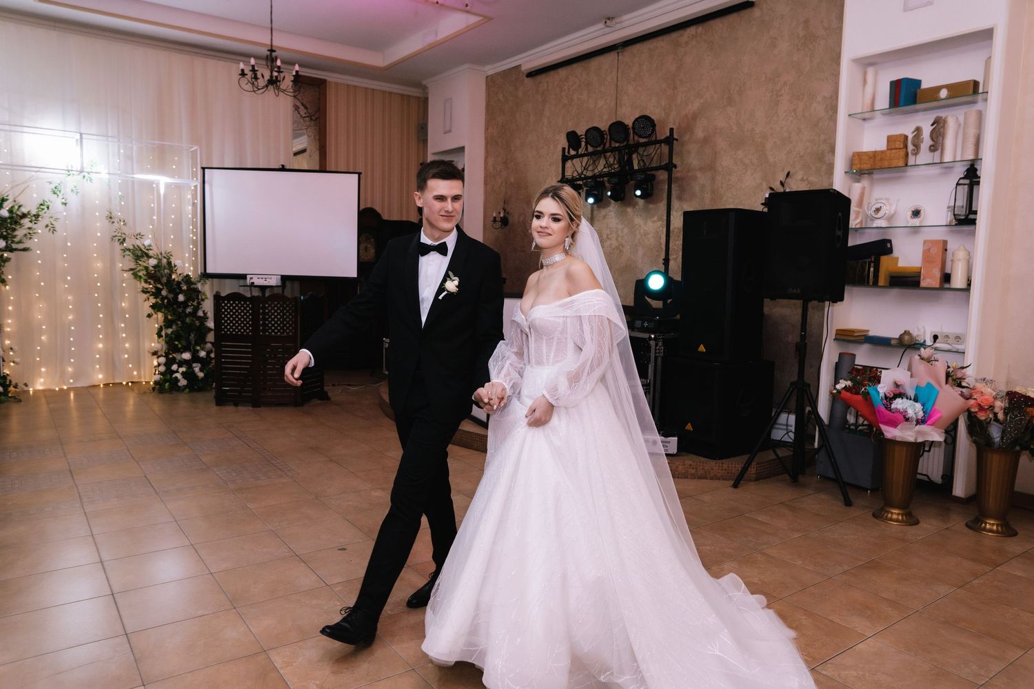 A couple dances together at their wedding reception in a beautifully lit ballroom with string lights and decor.