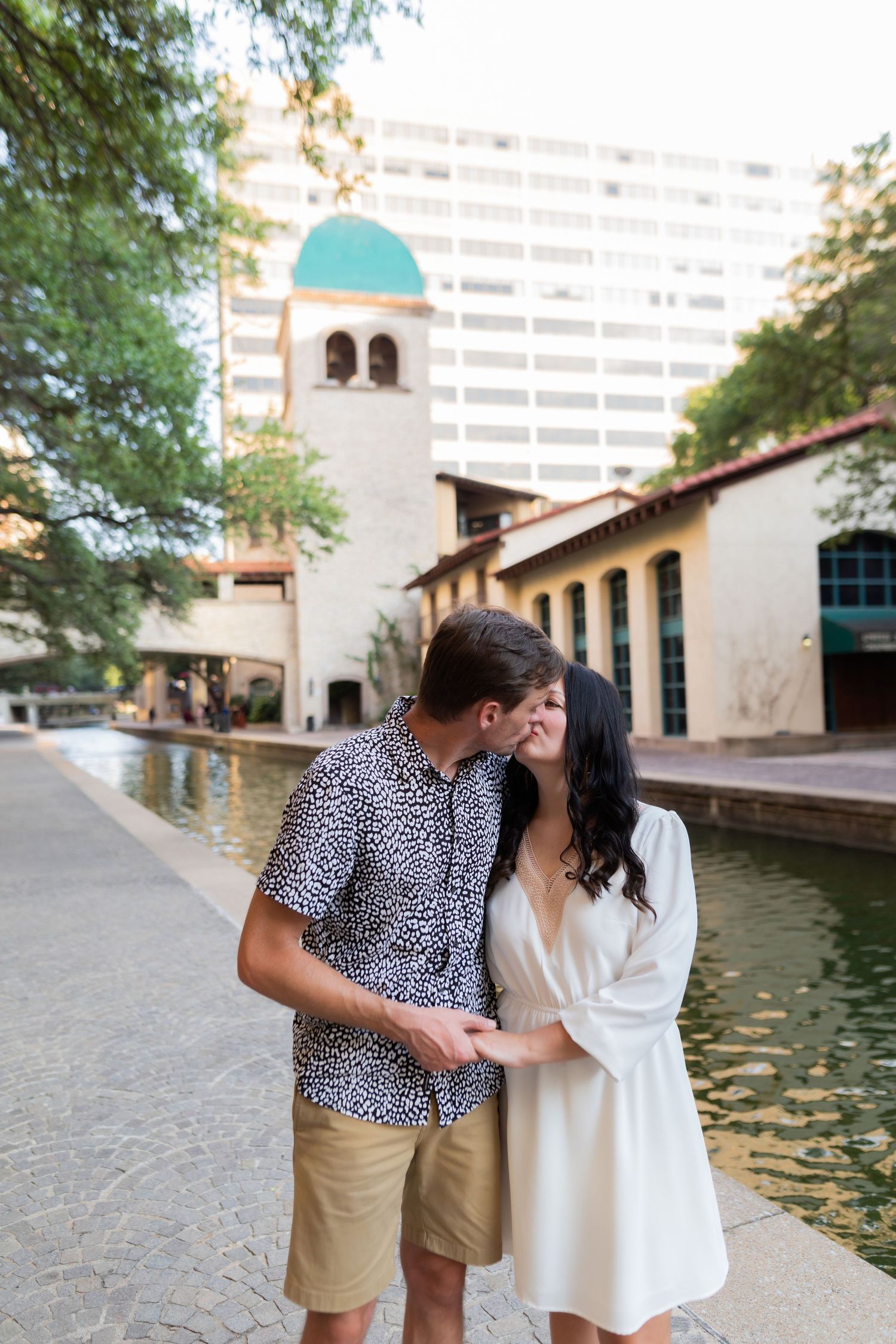 Couple shares romantic moments near a Spanish-style building with water features.