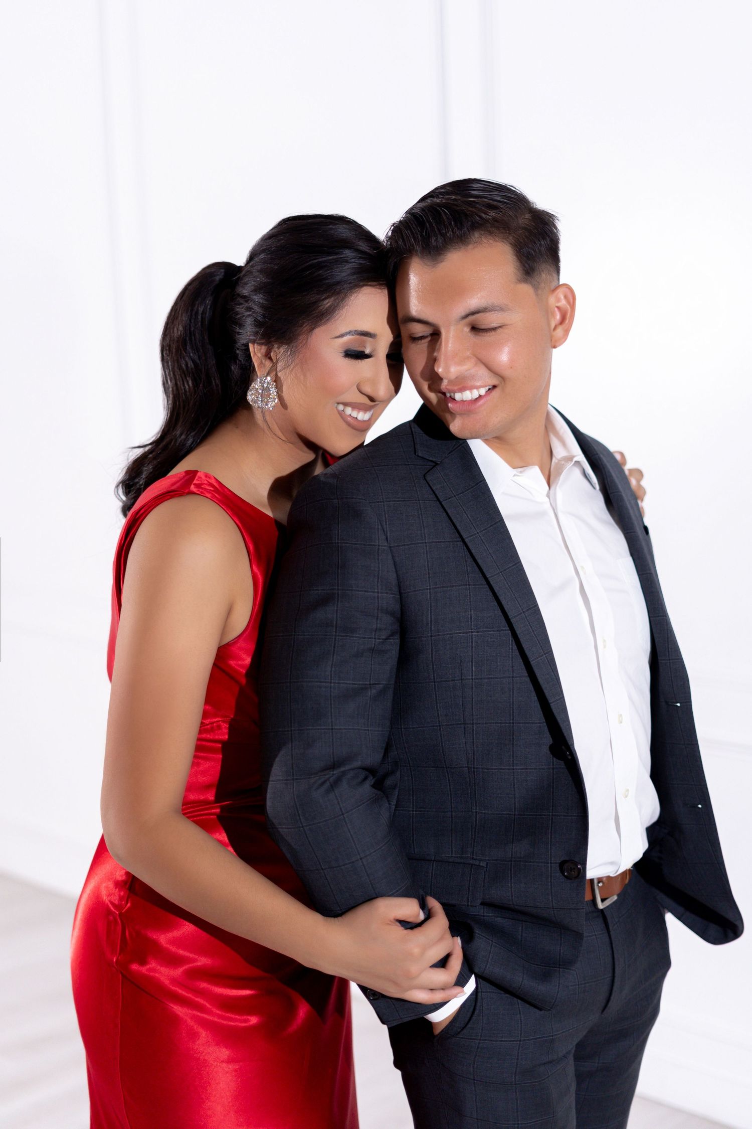 Couple in formal attire shares romantic moments against white backdrop.