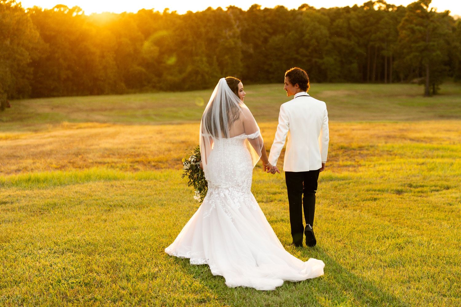 A romantic wedding photoshoot in a golden field at sunset with warm glowing light filtering through trees.