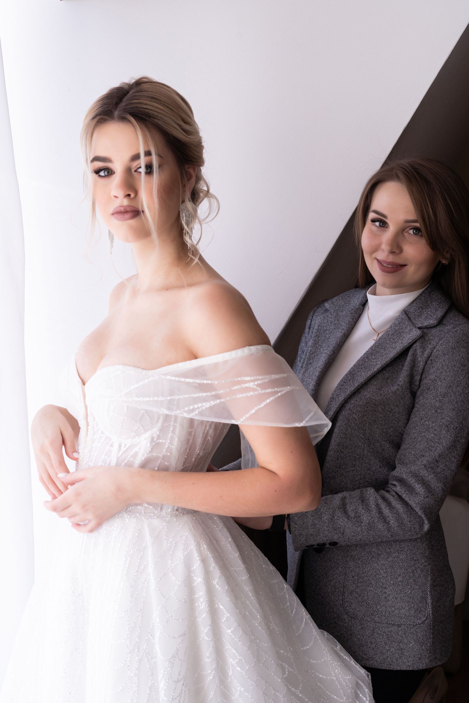 Professional maternity photoshoot featuring a white lace dress and grey blazer against a light backdrop.