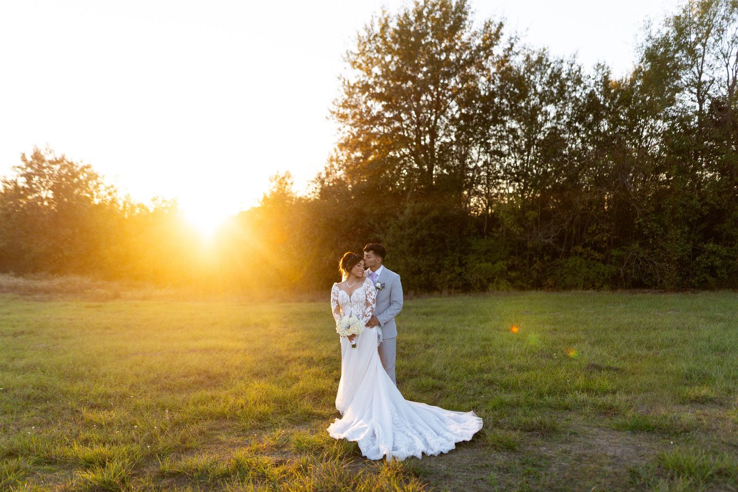 Wedding couple photographed in golden sunlit field during sunset.