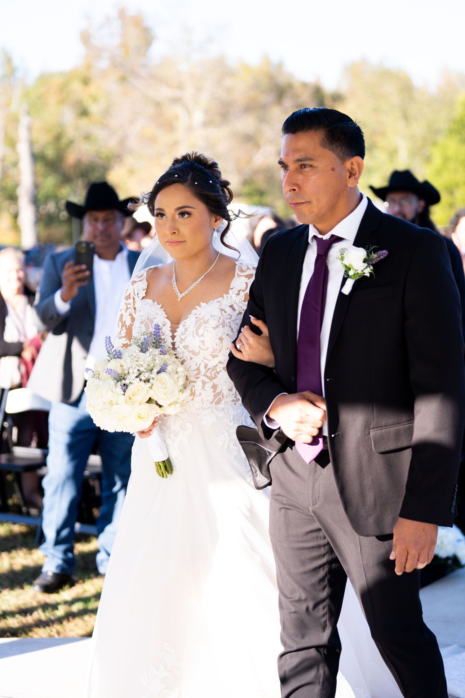 Outdoor wedding ceremony with couple walking down aisle while guests look on.