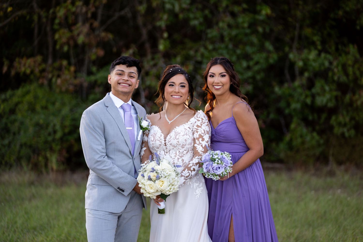 Wedding party poses together in elegant purple and gray attire against natural backdrop.