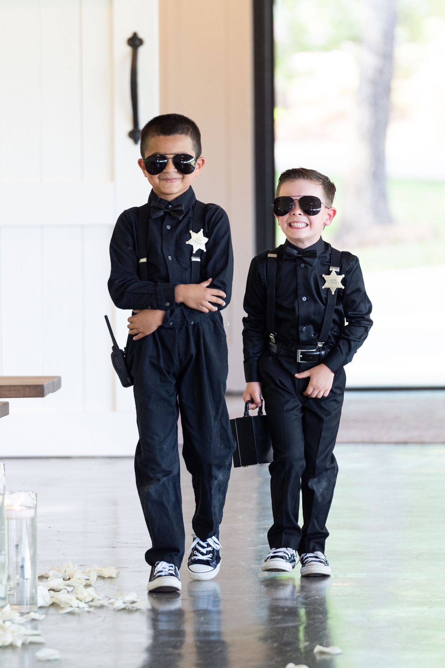Two young security officers in matching black uniforms and sunglasses stand confidently in a hallway.
