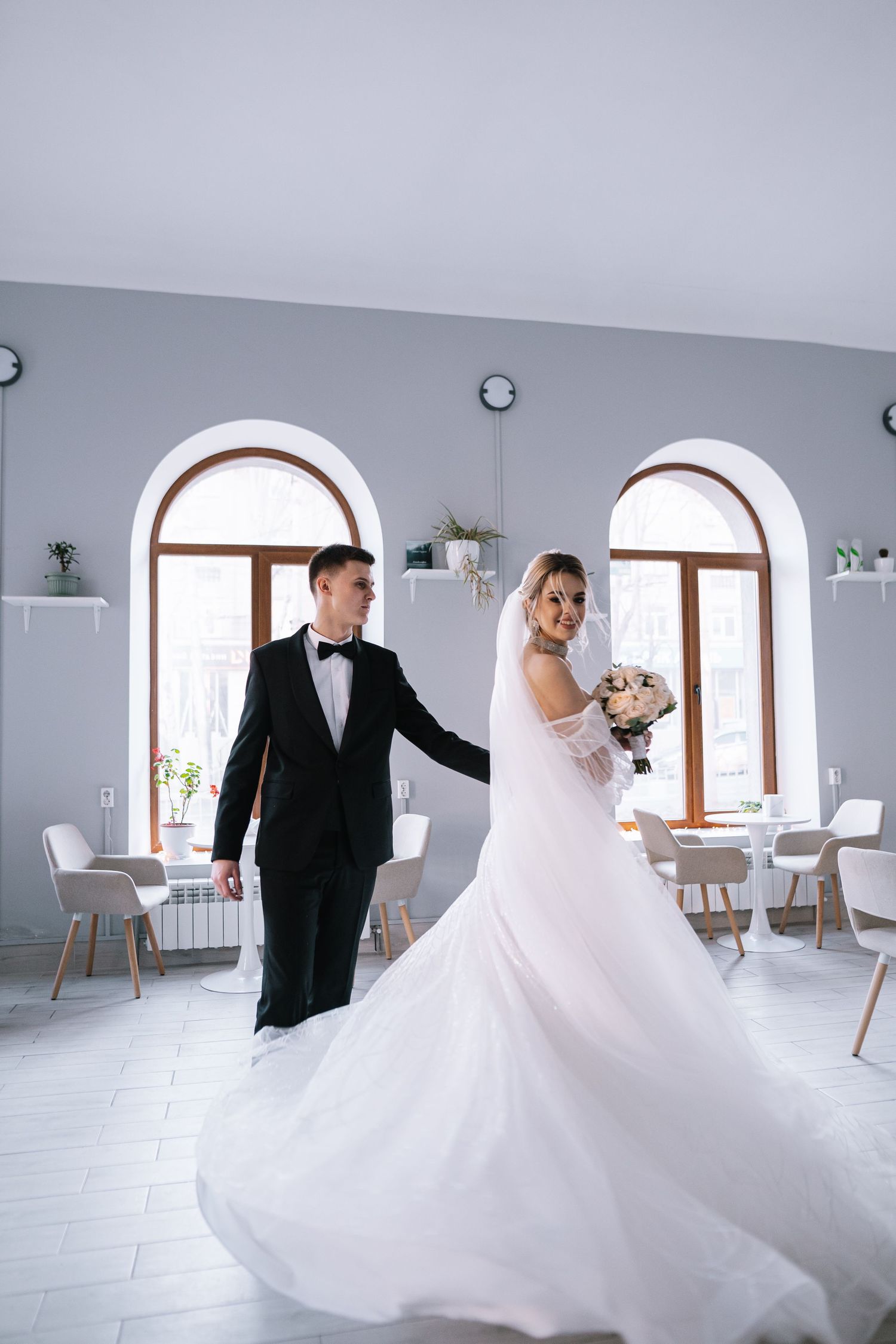 A wedding couple dances in a bright white room with arched windows as the bride's dress twirls elegantly.
