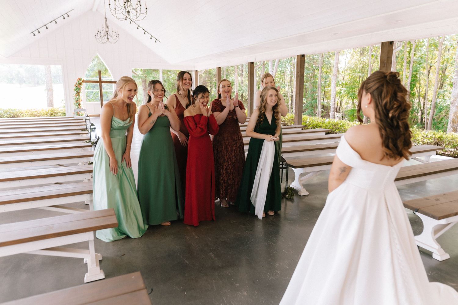 A group in formal dresses gathers at an outdoor covered venue with wooden benches in the background.