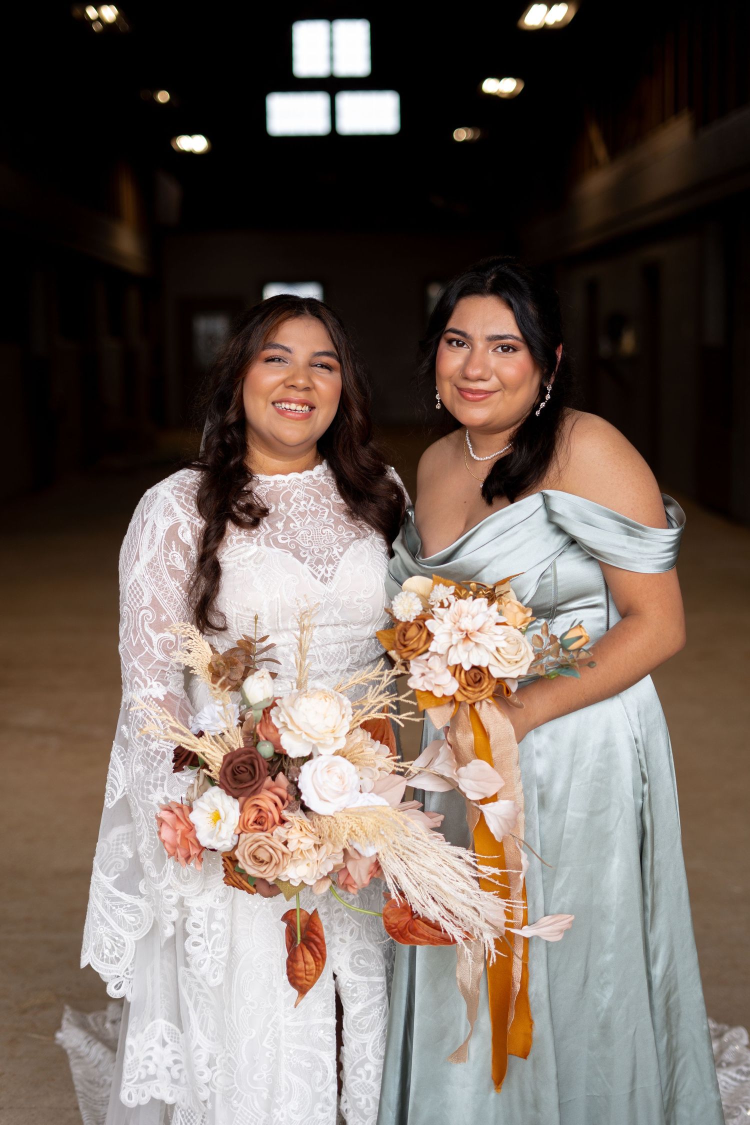 Wedding party holding bouquets with orange and cream flowers pose together indoors.