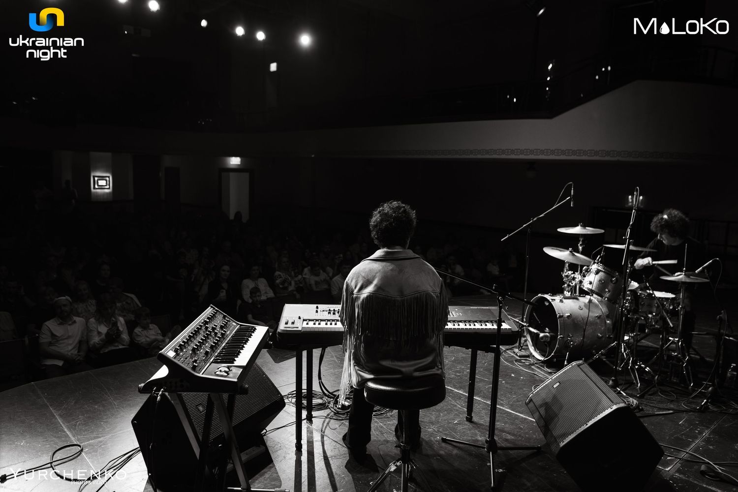 Wide panoramic view of musicians performing on dimly lit concert stage.