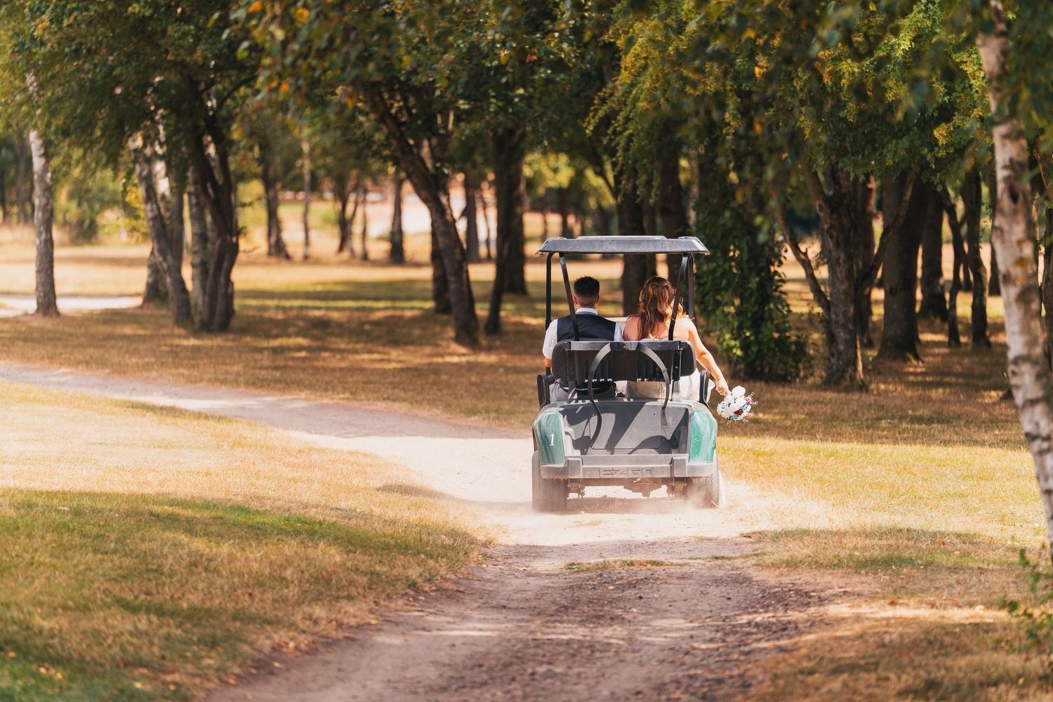 Golf cart driving along a scenic tree-lined dirt path on a sunny day.