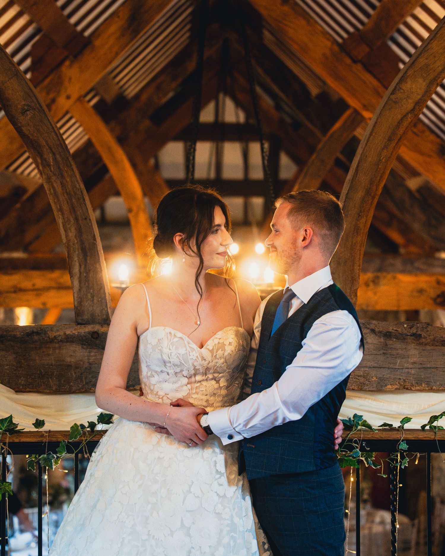 Bride and groom share a romantic moment in a rustic barn wedding venue with warm glowing lights.