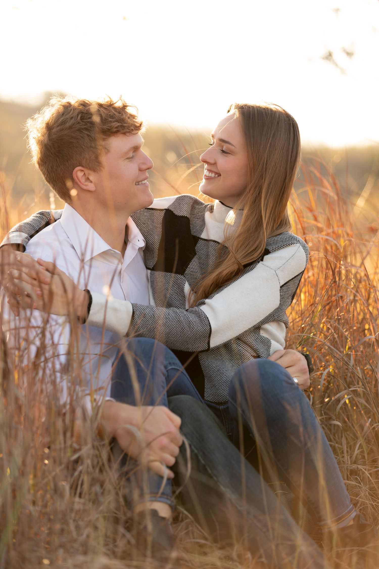 Happy young couple sitting together in tall golden grass during sunset.