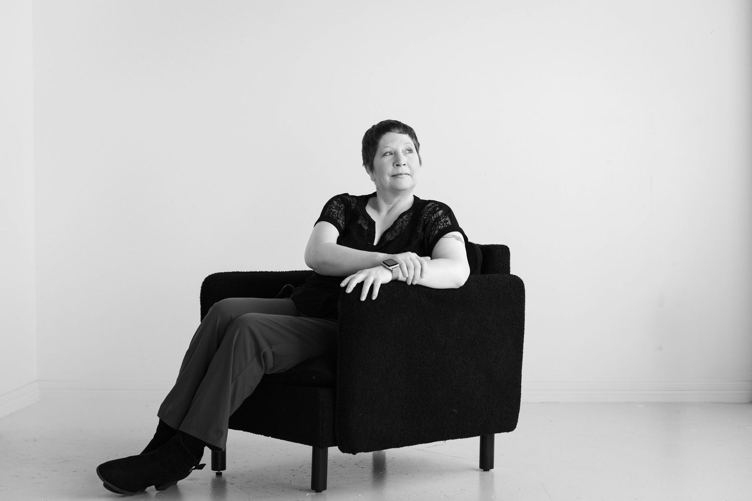 Elegant black and white photo of a woman posed confidently in a sleek black chair in a minimalist studio.