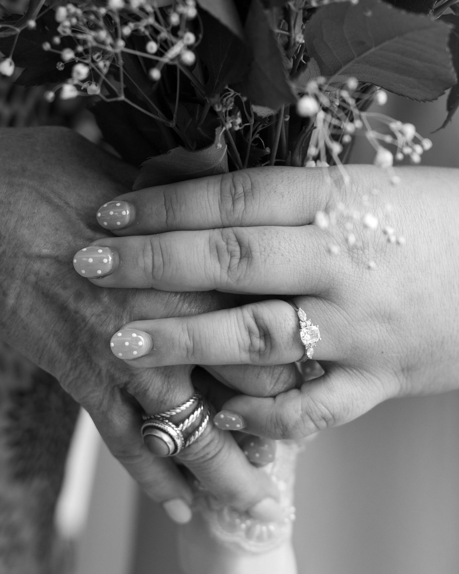 Black and white close-up of bride and mother holding hands with wedding rings visible.