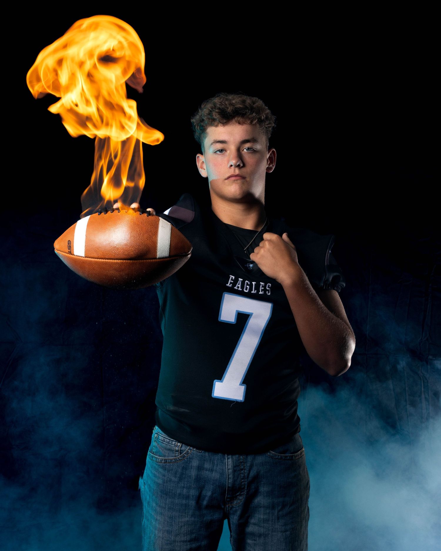 Football player in Eagles jersey number 7 holds a flaming football in a dramatic blue smoke studio photo.