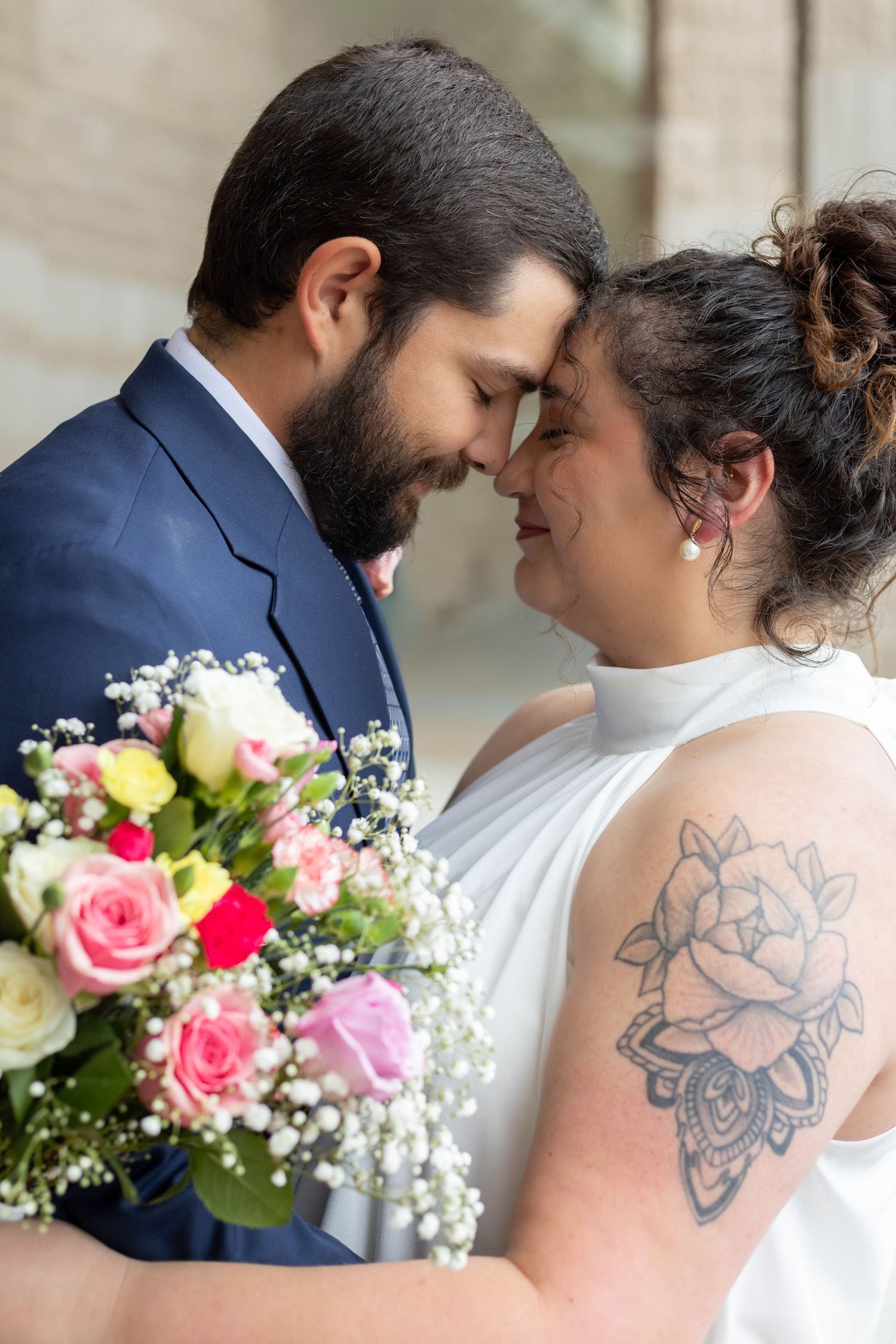 Bride and groom touching foreheads romantically while holding colorful wedding bouquet.