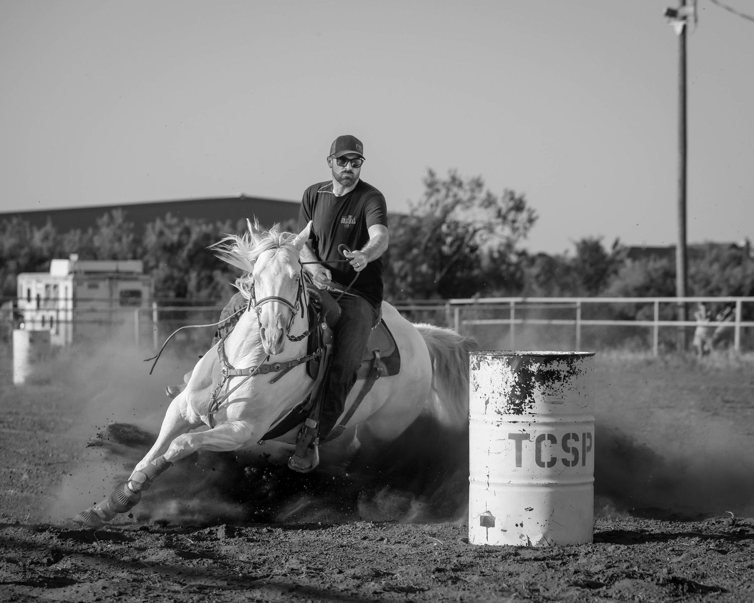 Black and white photo of a rider on a horse turning around a barrel during a barrel racing event.