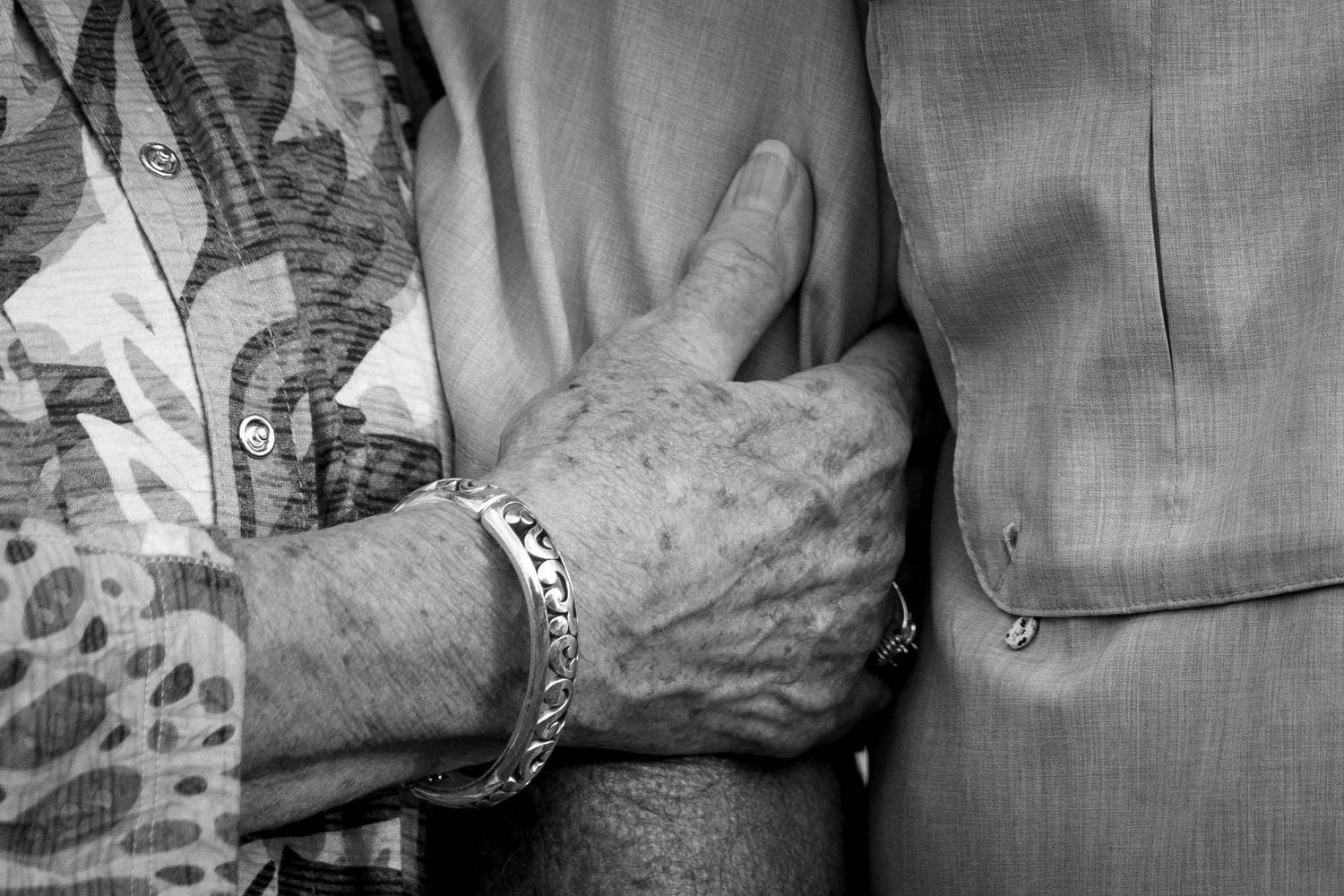 Close-up black and white photo of elderly couple holding arms together.