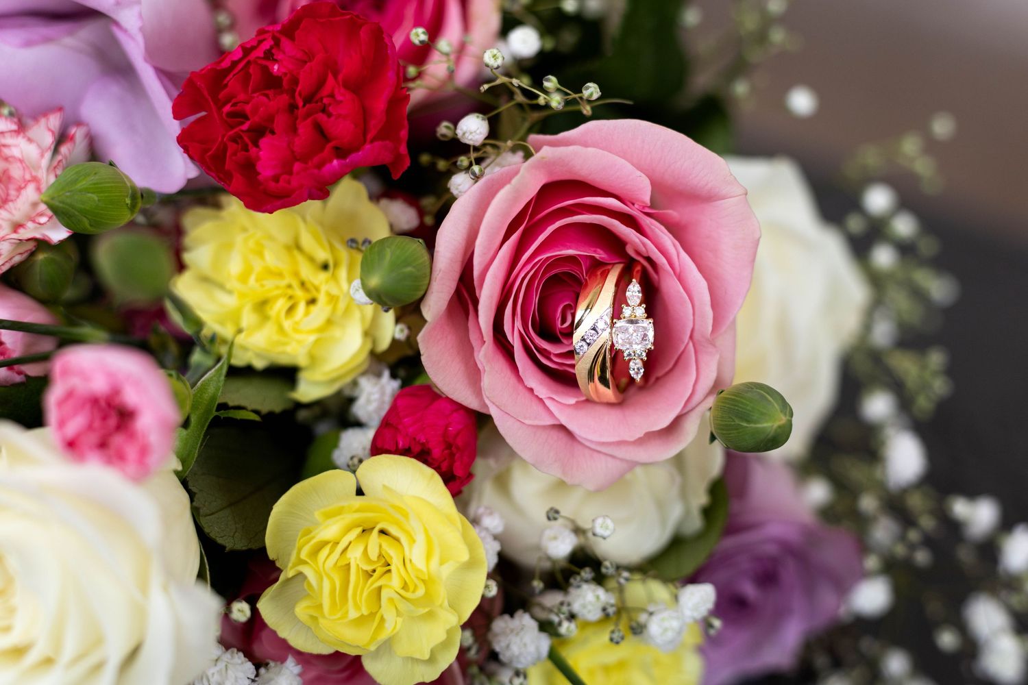 Wedding rings nestled inside a pink rose in a colorful bridal bouquet.