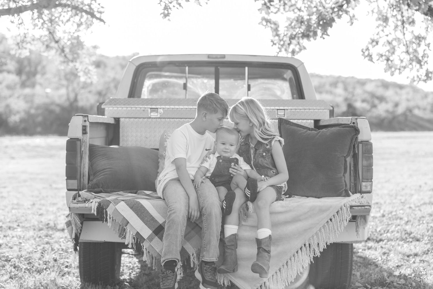 Black and white photo of young family sitting on vintage truck tailgate.