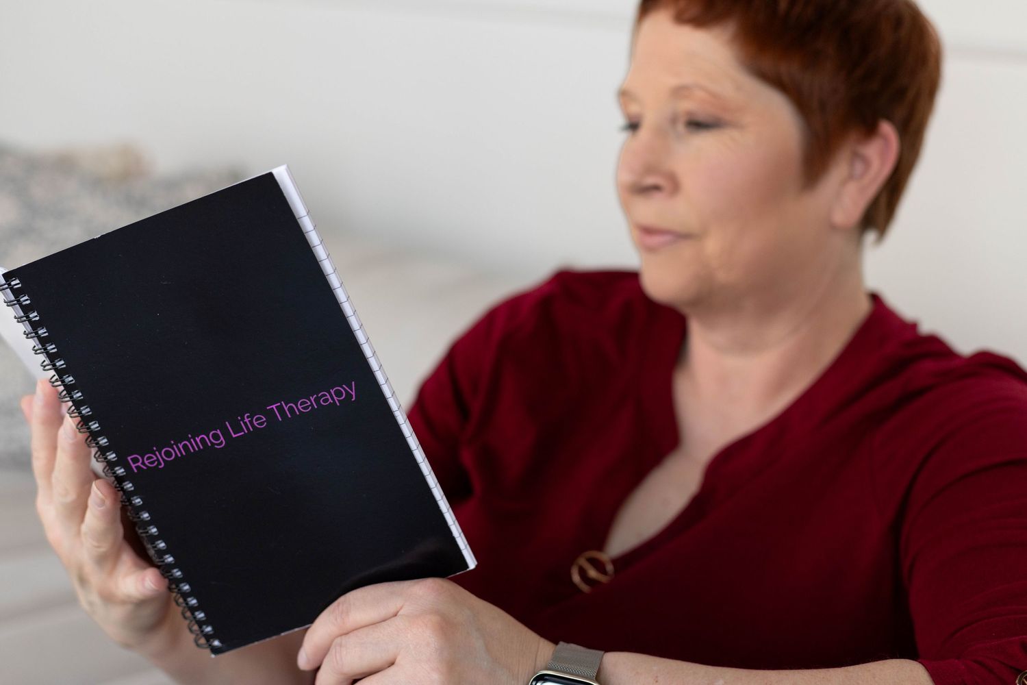 Woman in red sweater reading Rejoining Life Therapy notebook in soft focus portrait photo.