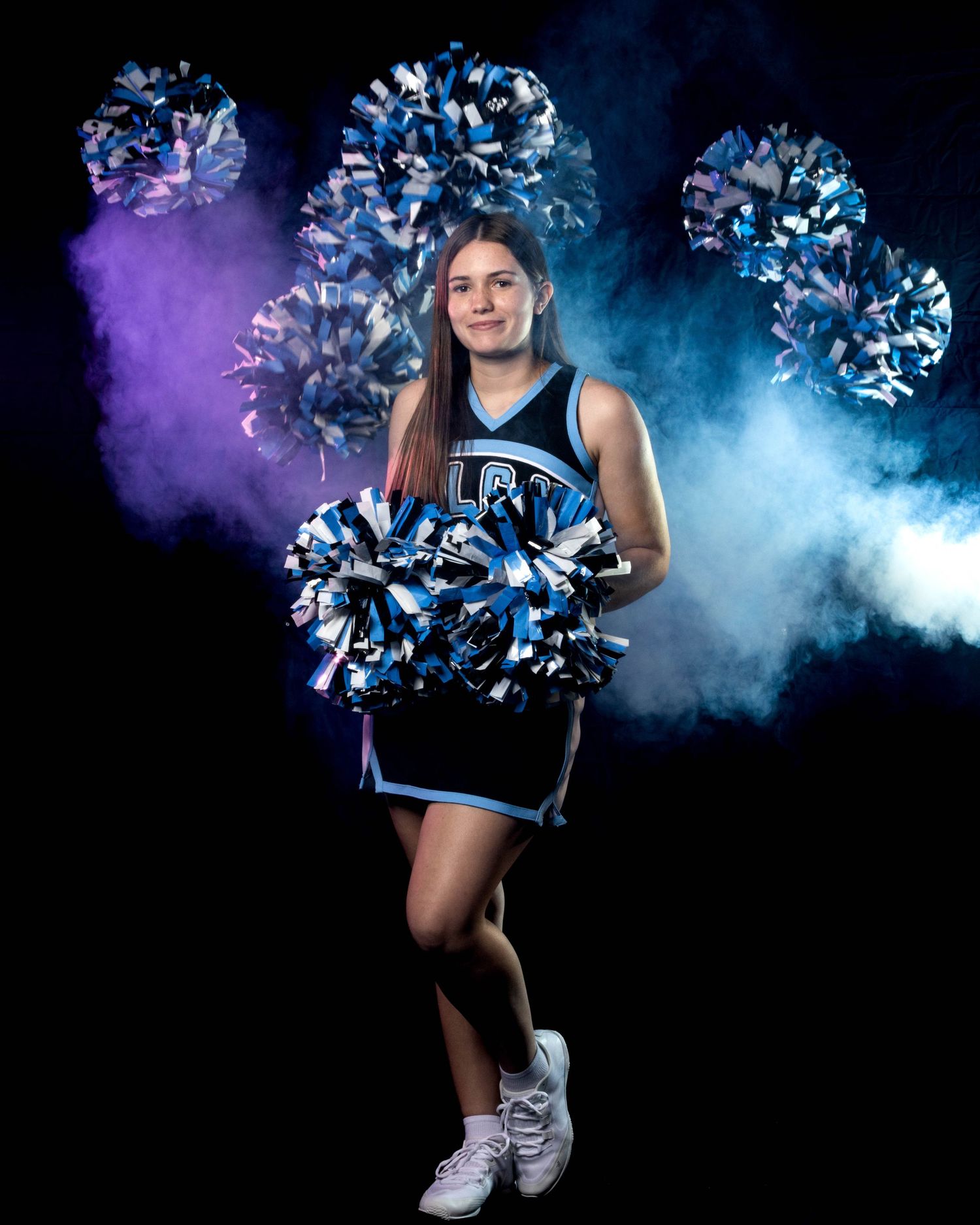 Cheerleader in blue LCA uniform poses with multiple pom-poms in a purple and blue smoky studio photo.