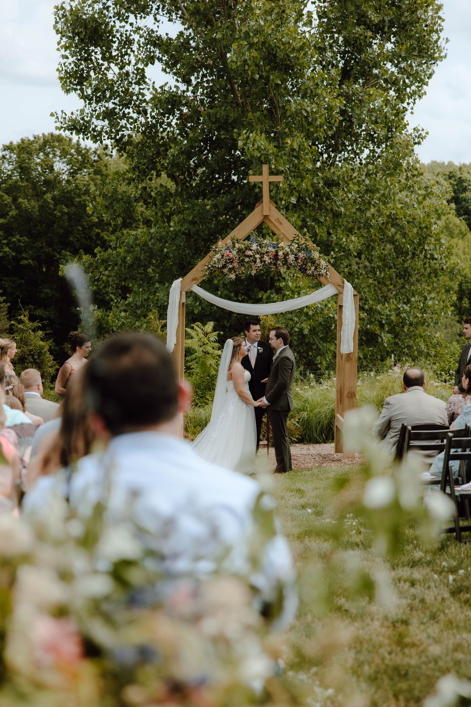 Couple exchanging vows at outdoor wedding ceremony under wooden cross arch.