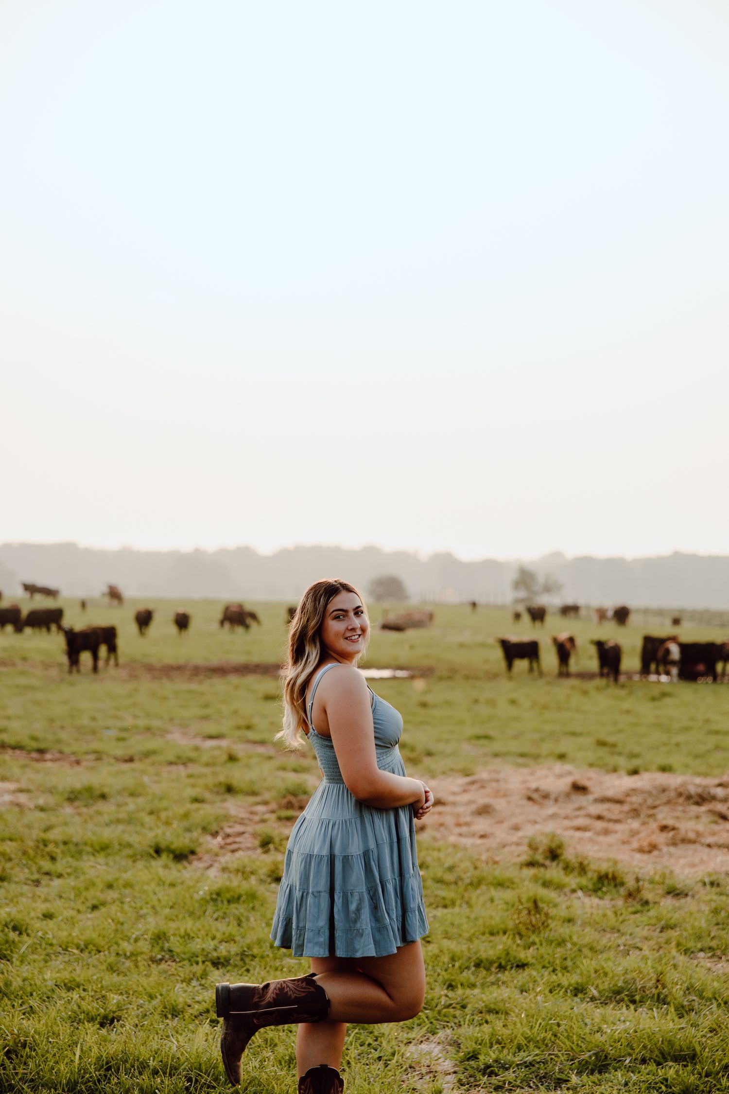 A blue sundress stands out against a pastoral scene with cattle grazing in the background.