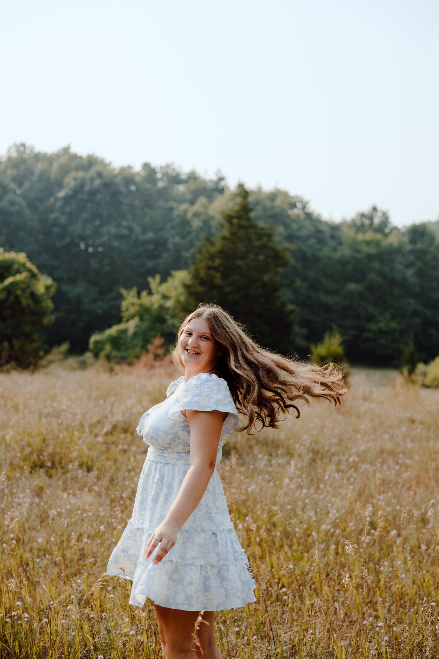 A person in a white dress twirls playfully in a sunlit meadow during golden hour.