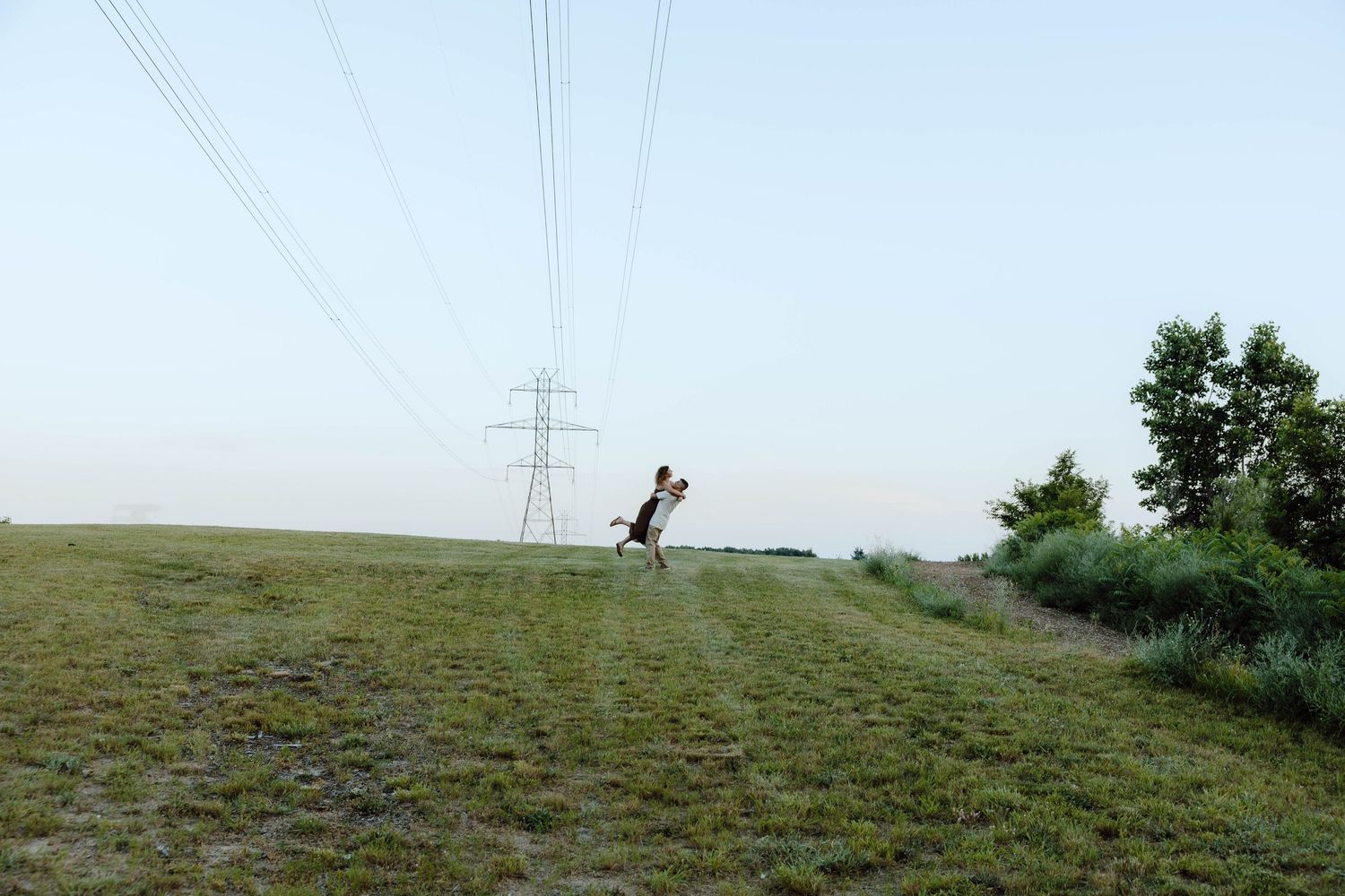 Person running on a grassy hill beneath large power lines and transmission tower in an open field.