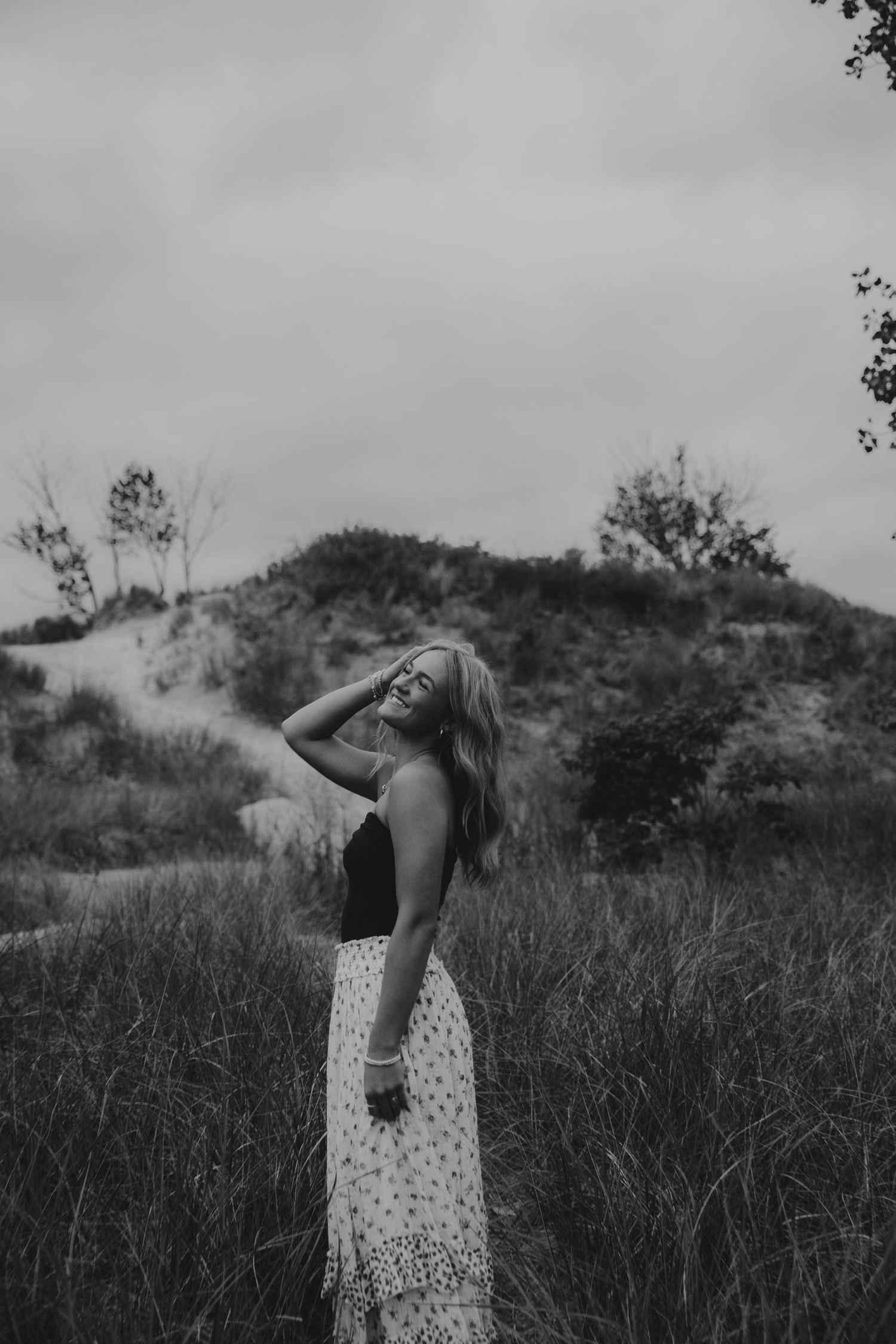 Artistic black and white photo of someone dancing in a meadow with dramatic sky.
