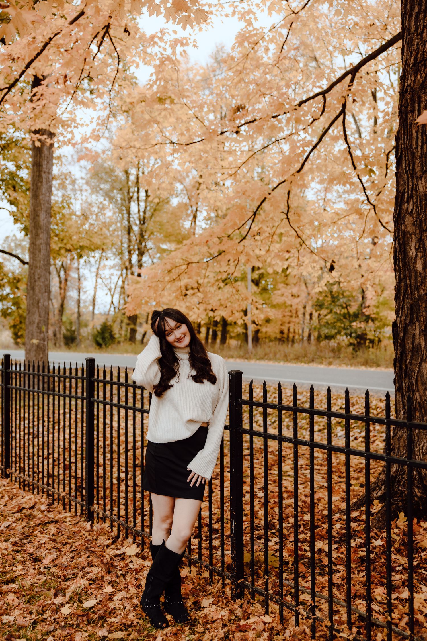 Autumn portrait session featuring iron fence and golden fall foliage in the background.