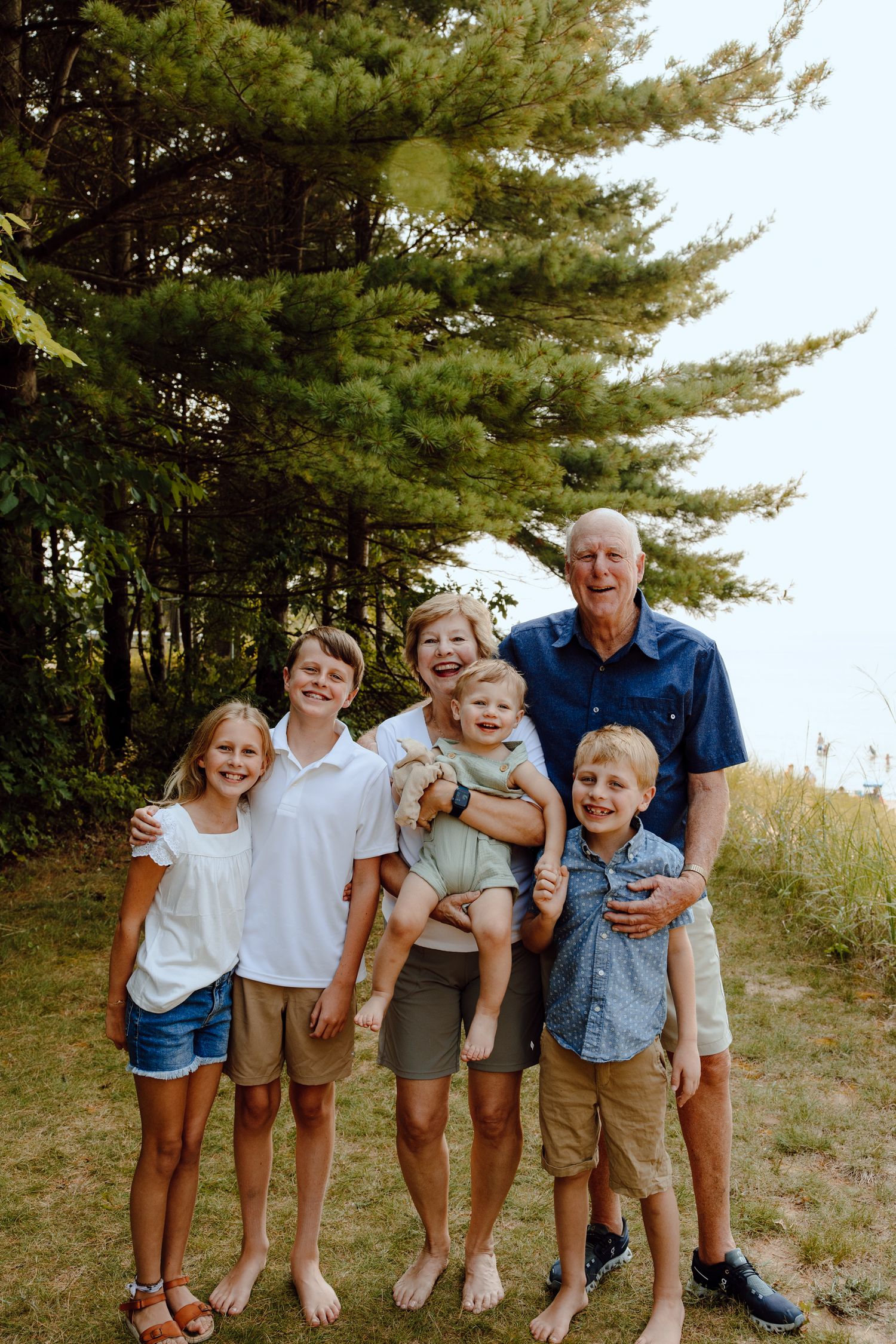 Family group poses casually together under tall pine trees on a hillside.