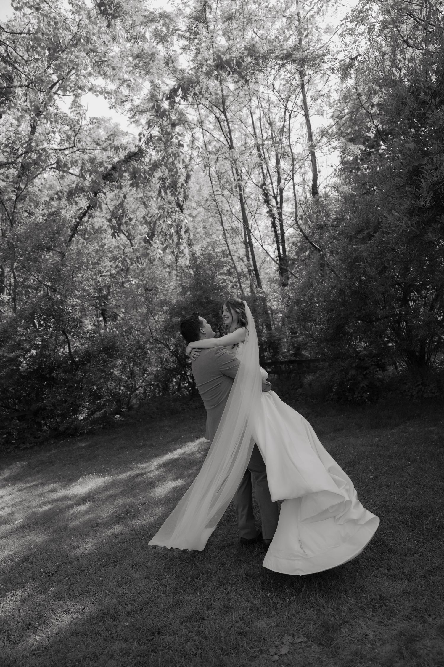 Bride and groom share a romantic dance outdoors in a lush garden, captured in black and white photography.
