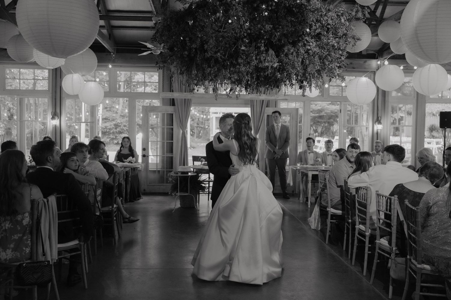 Black and white photo of a bride dancing with a guest at an elegant wedding reception with lantern decorations.
