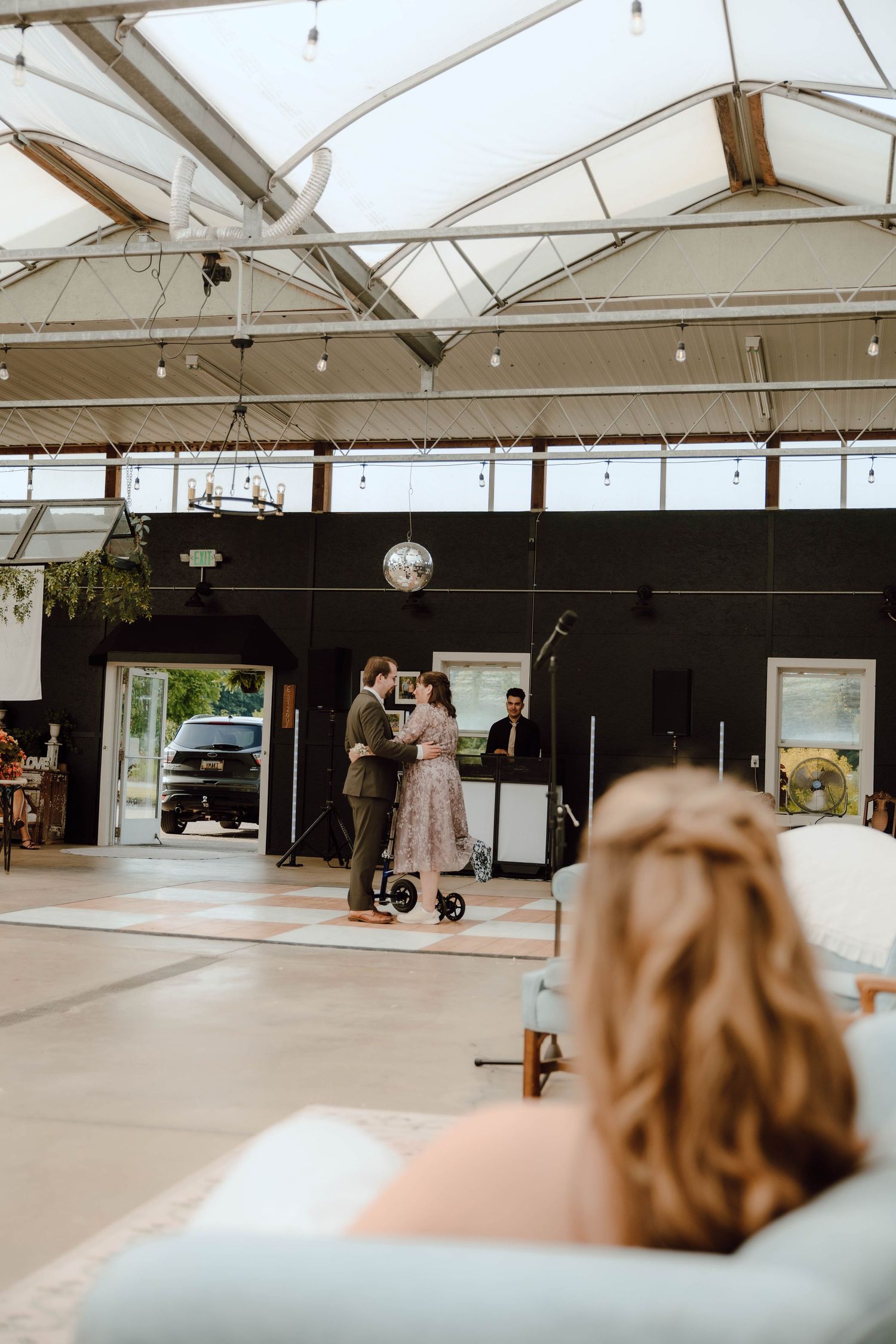 Couple sharing dance in modern wedding reception venue with disco ball and string lights.