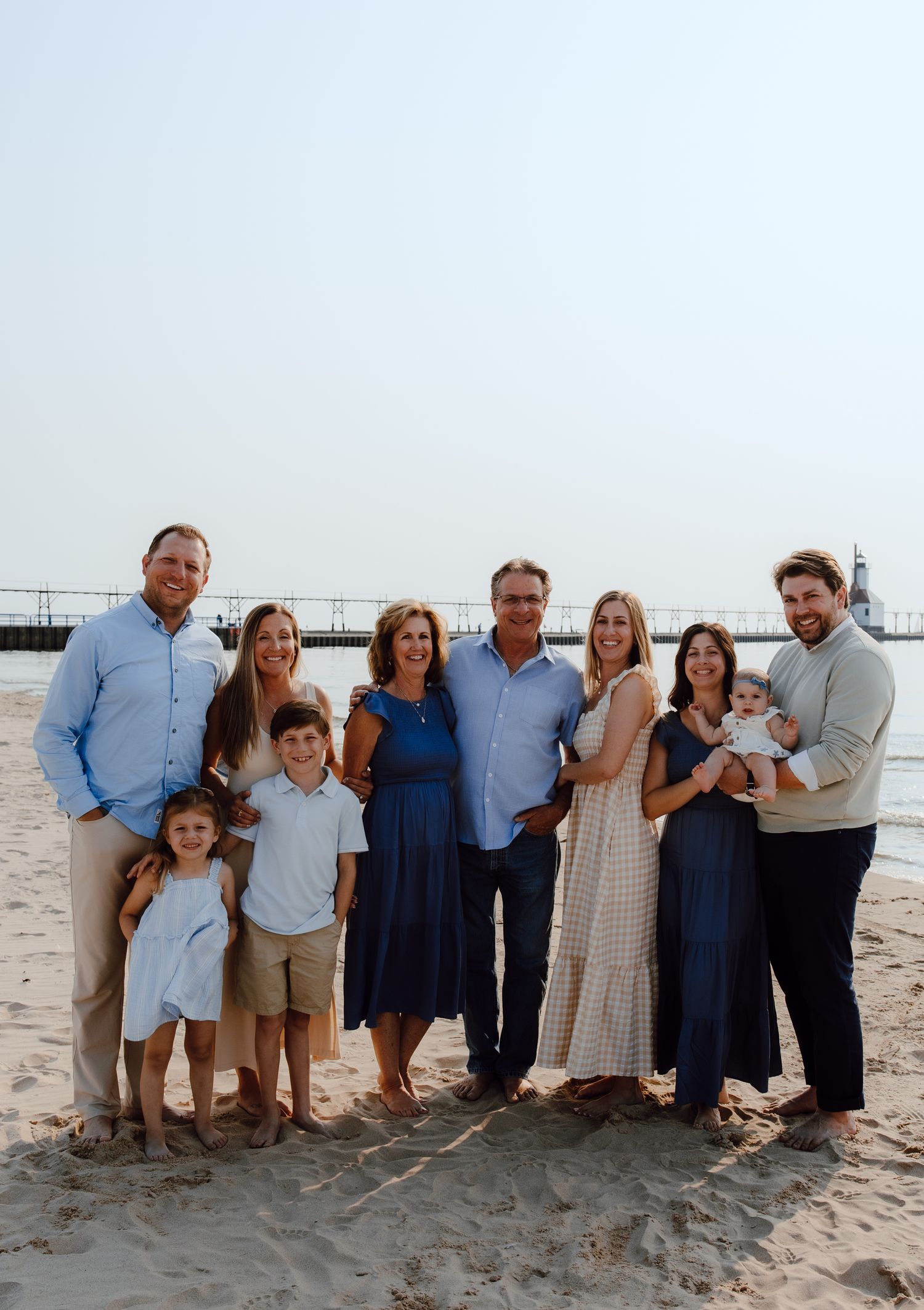 Extended family portrait on a beach at sunset with a pier in the background.