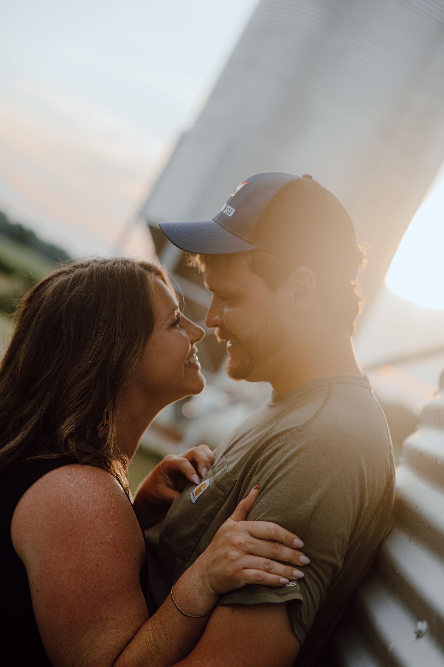 A couple shares an intimate moment in warm sunlight with industrial equipment in background.