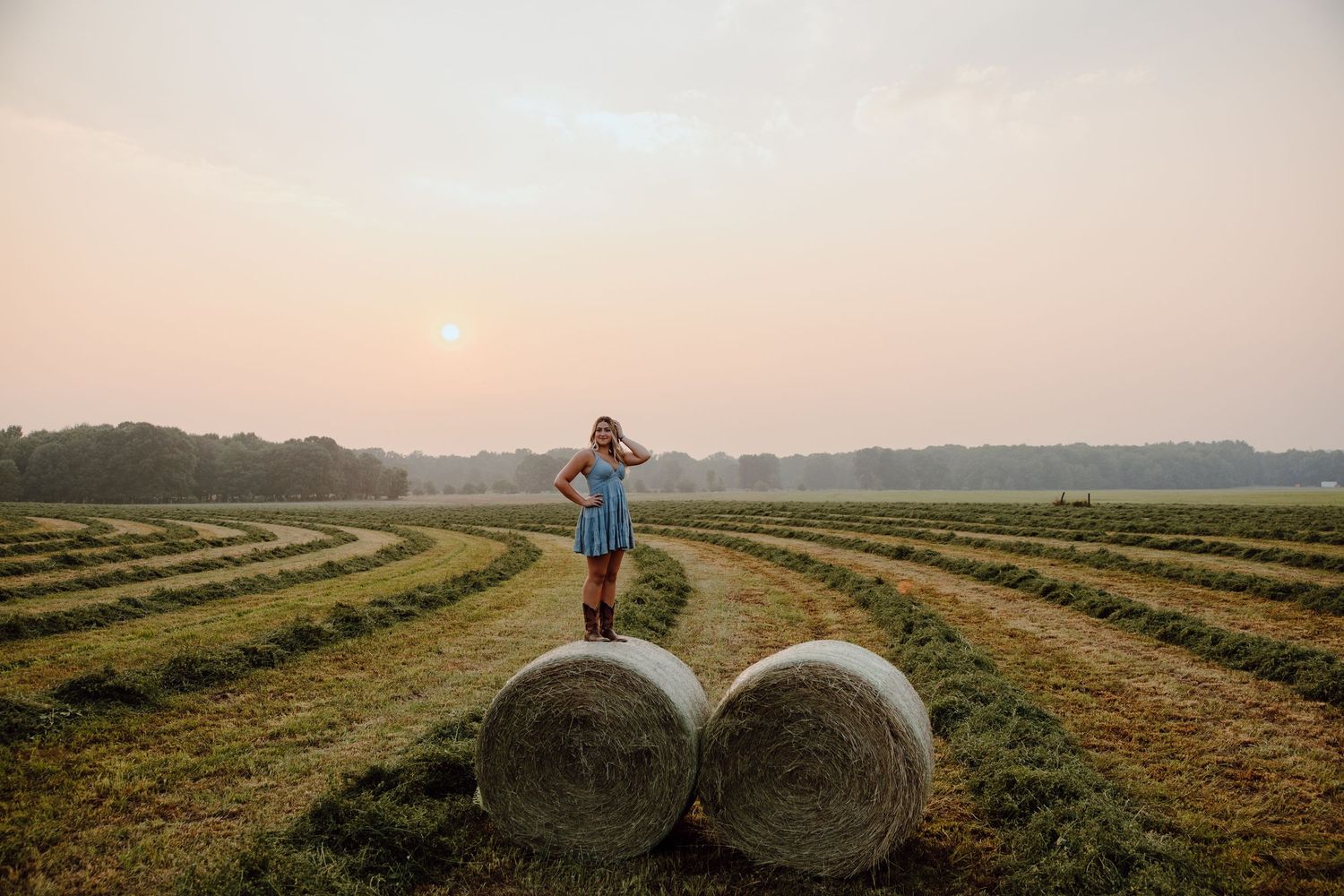 Round hay bales line up in rows across a farm field at sunset.
