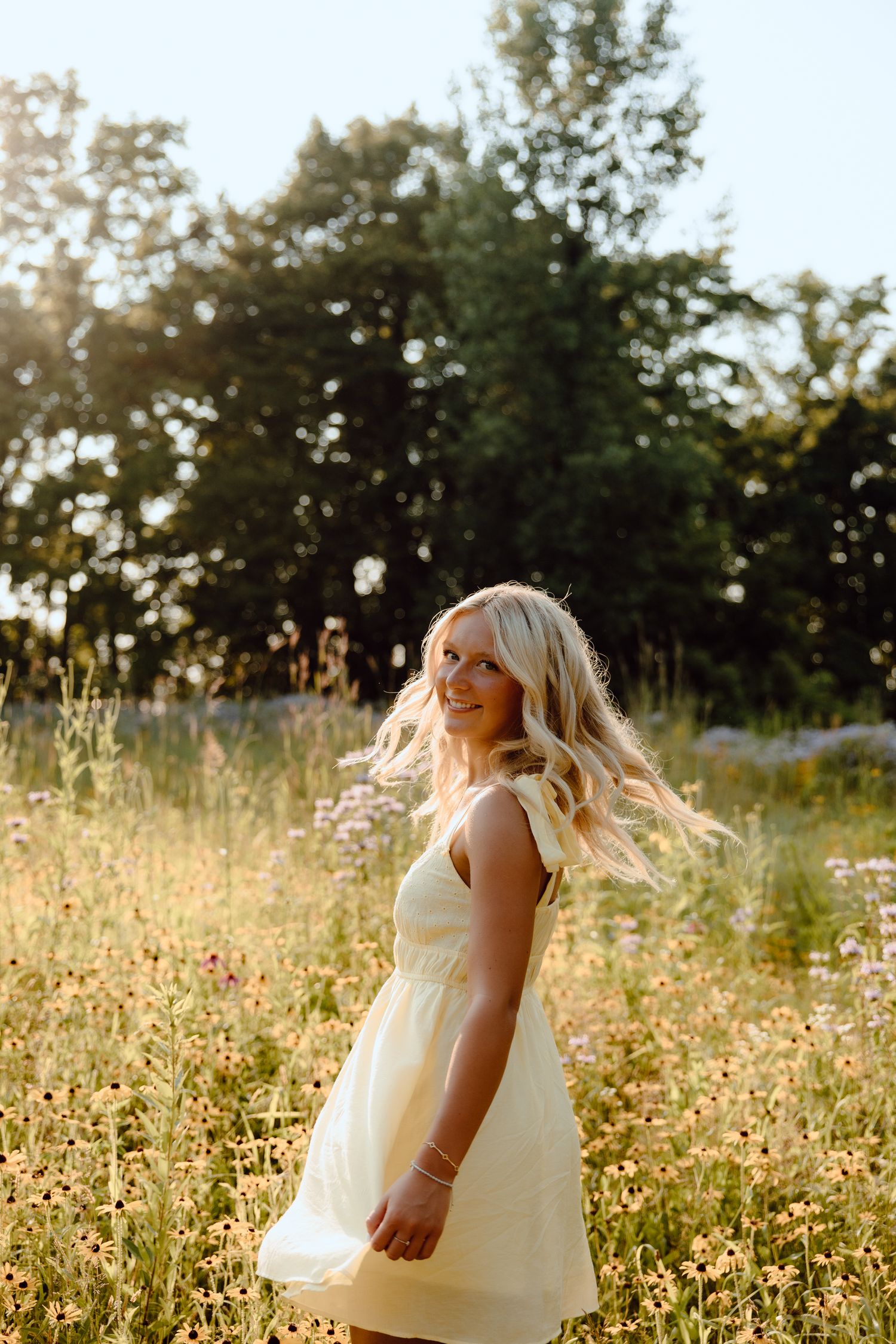A light and airy portrait in a sunny meadow with wildflowers and trees in the background.