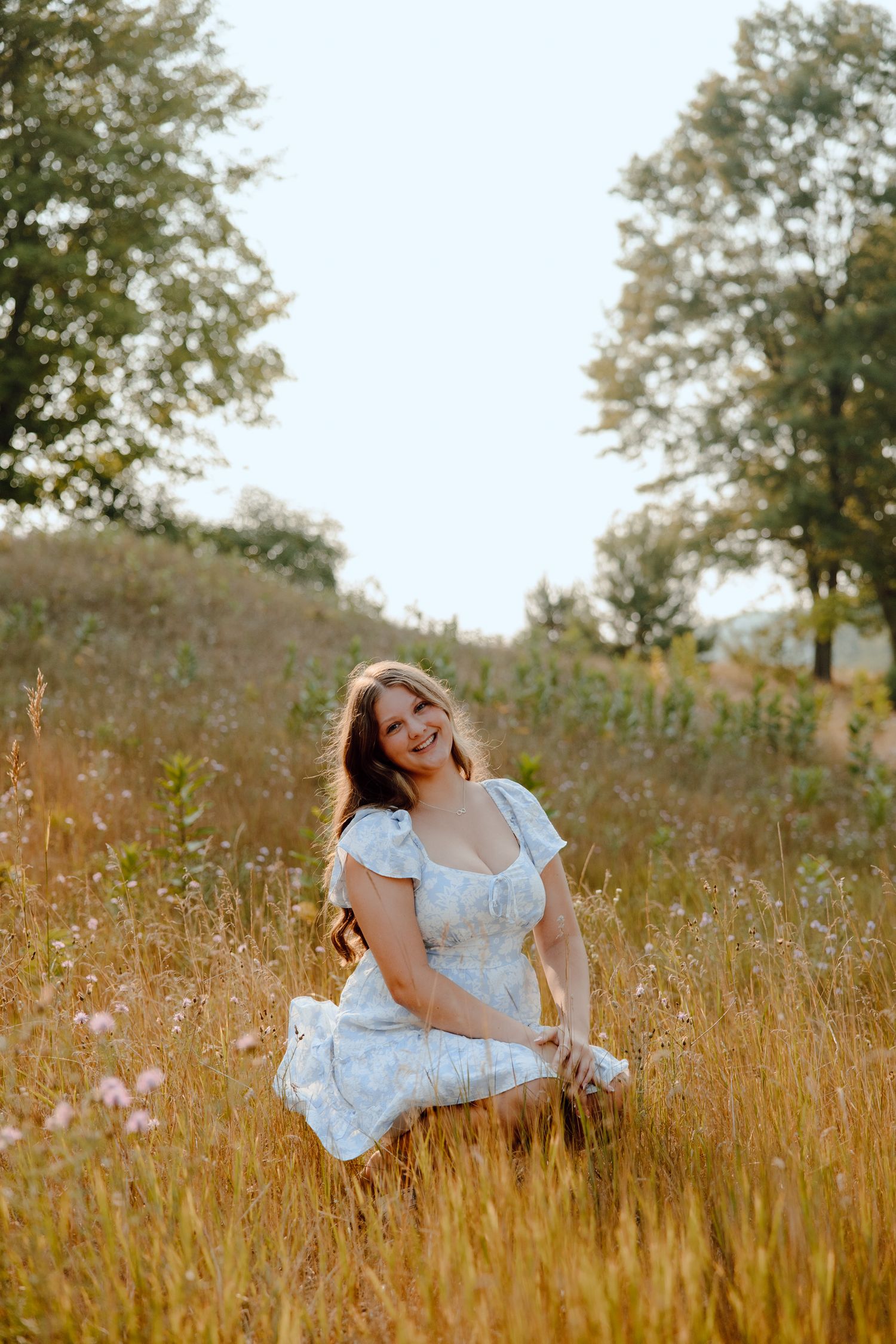 A person in a white dress reclines gracefully among tall grass in a summer meadow.