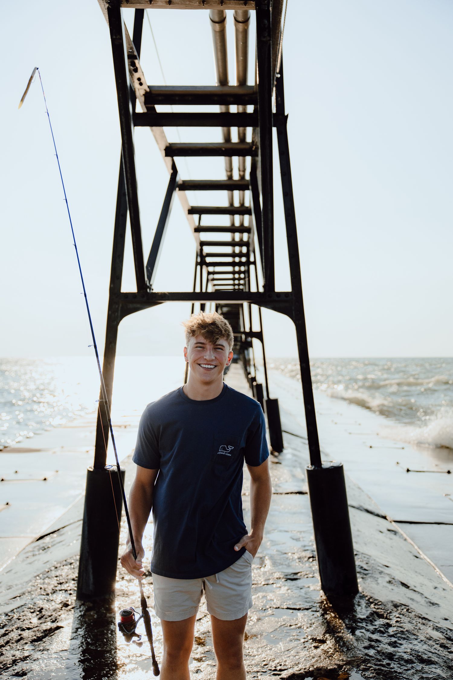 Person standing under a wooden pier structure near the ocean.
