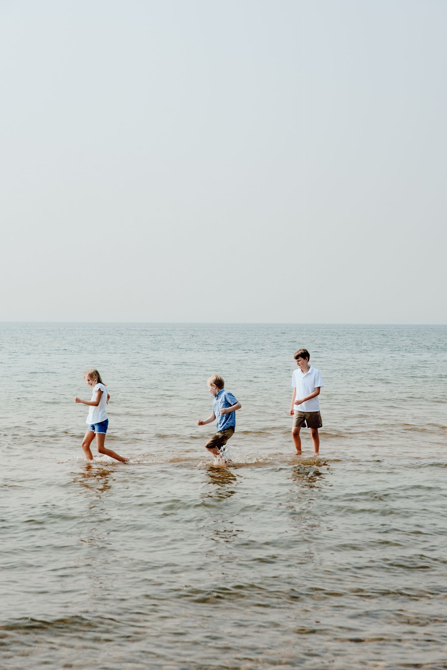 Three people splashing and playing in shallow ocean water on a bright day.