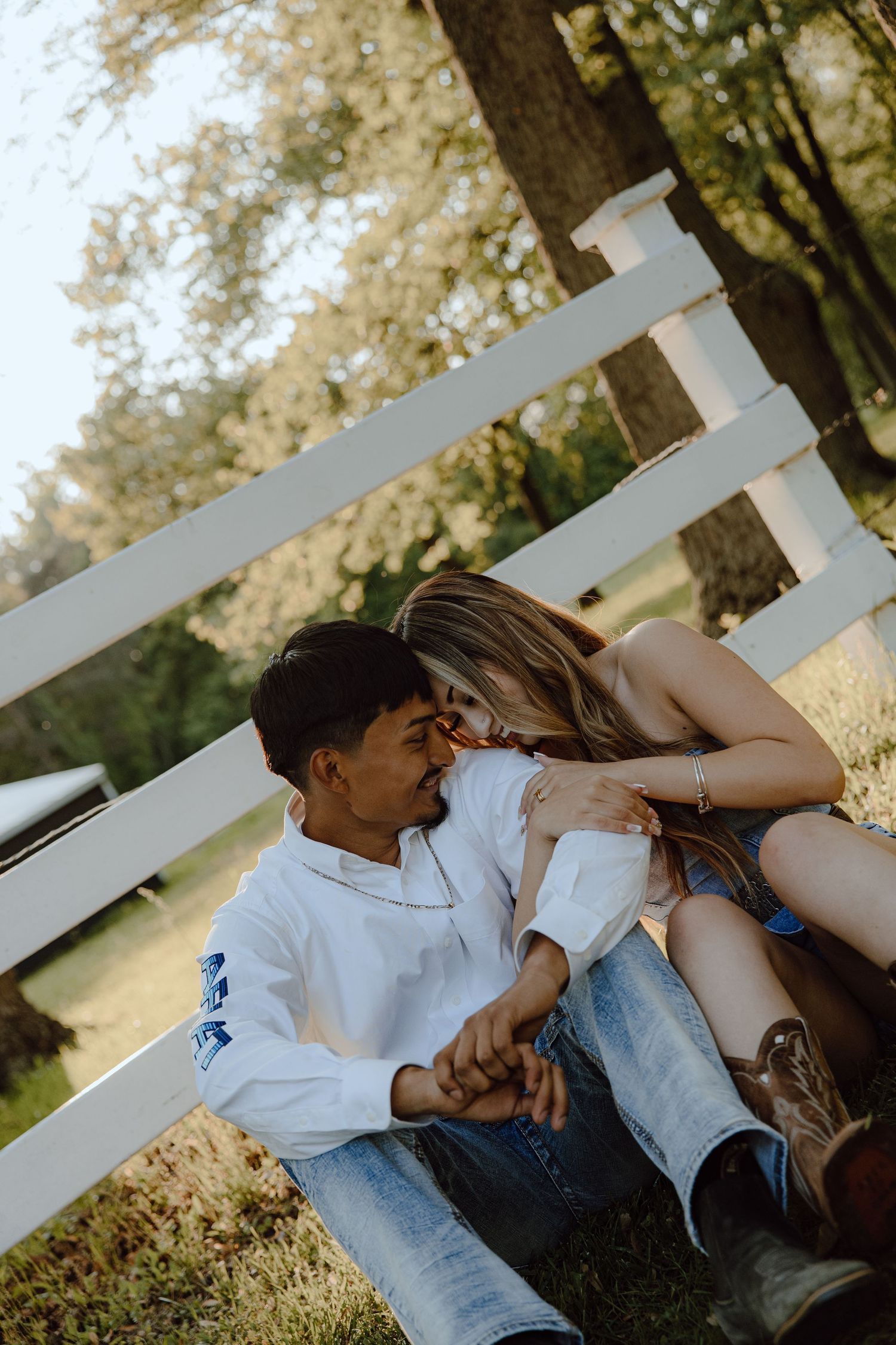 A couple embraces while sitting on a white fence during sunset.