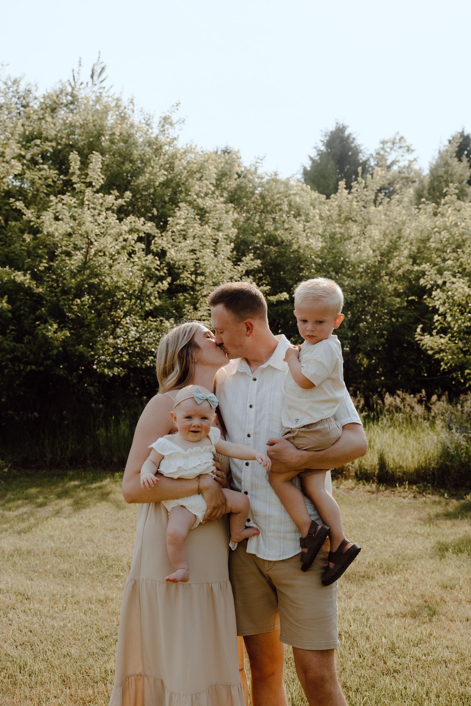 Family of four posing for a portrait in front of blooming bushes during golden hour.