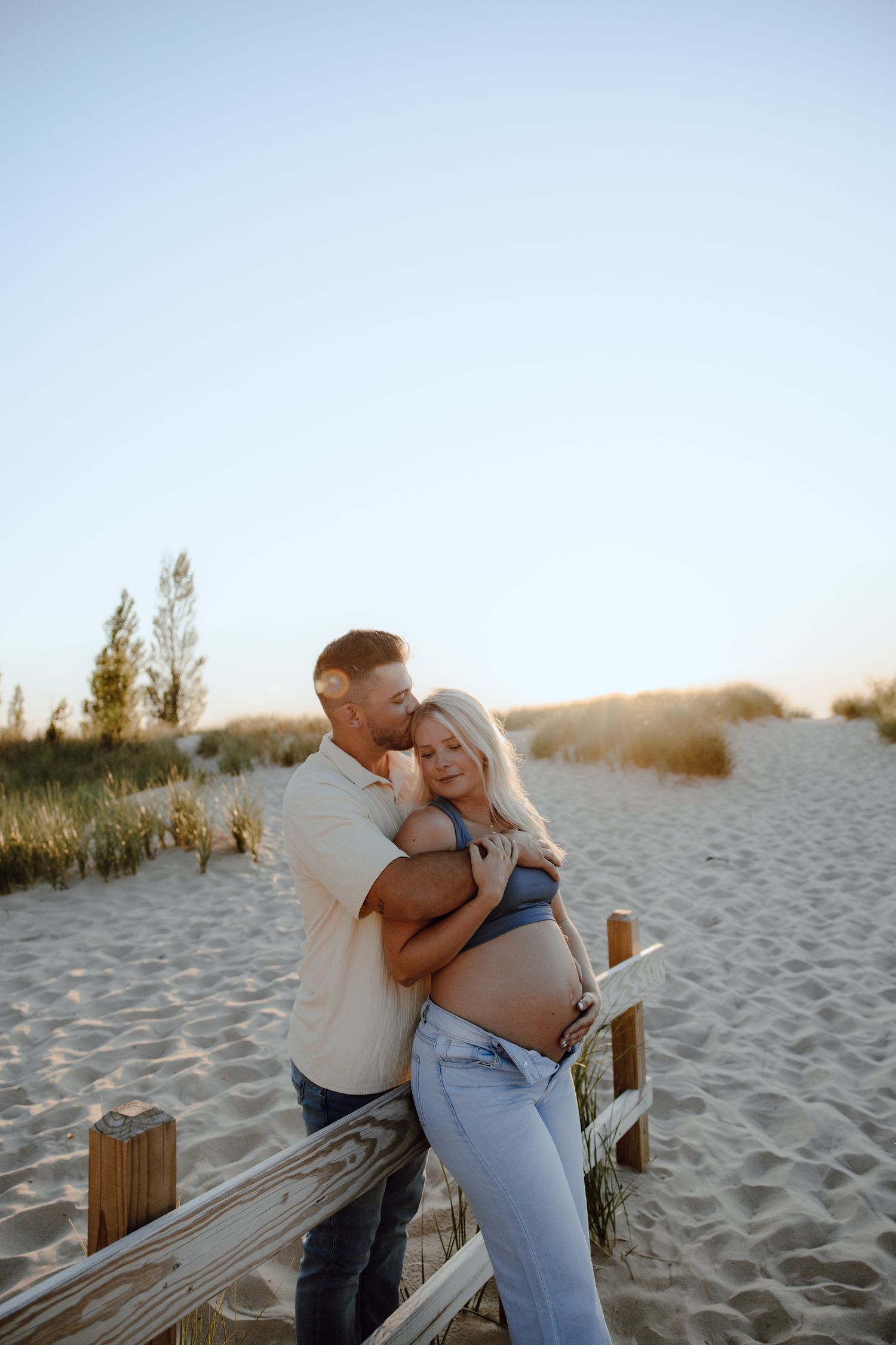 Couple sharing intimate moments along a wooden boardwalk at the beach during golden hour.